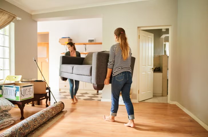 Two women carrying sofa out of a house